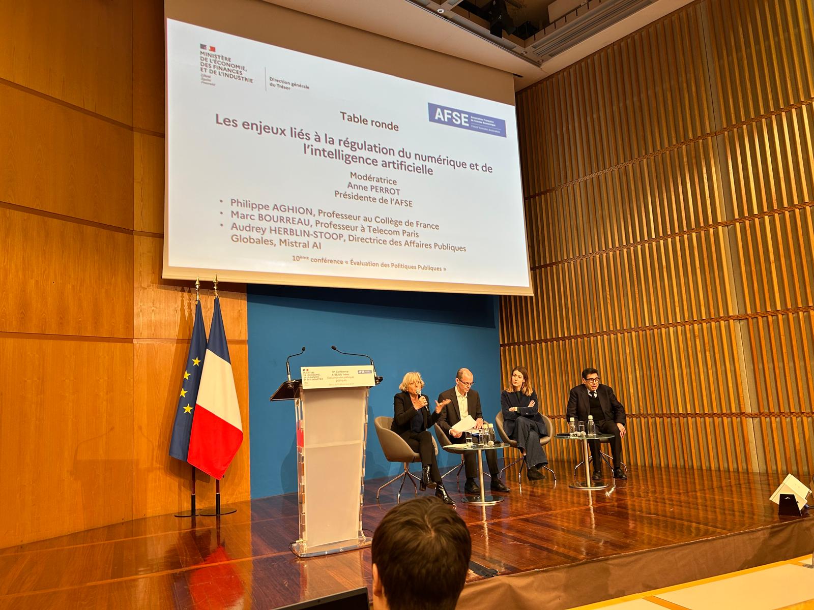 Panel discussion on stage at the AFSE conference, with a slide about the regulation of digital technology and AI displayed behind the panelists.